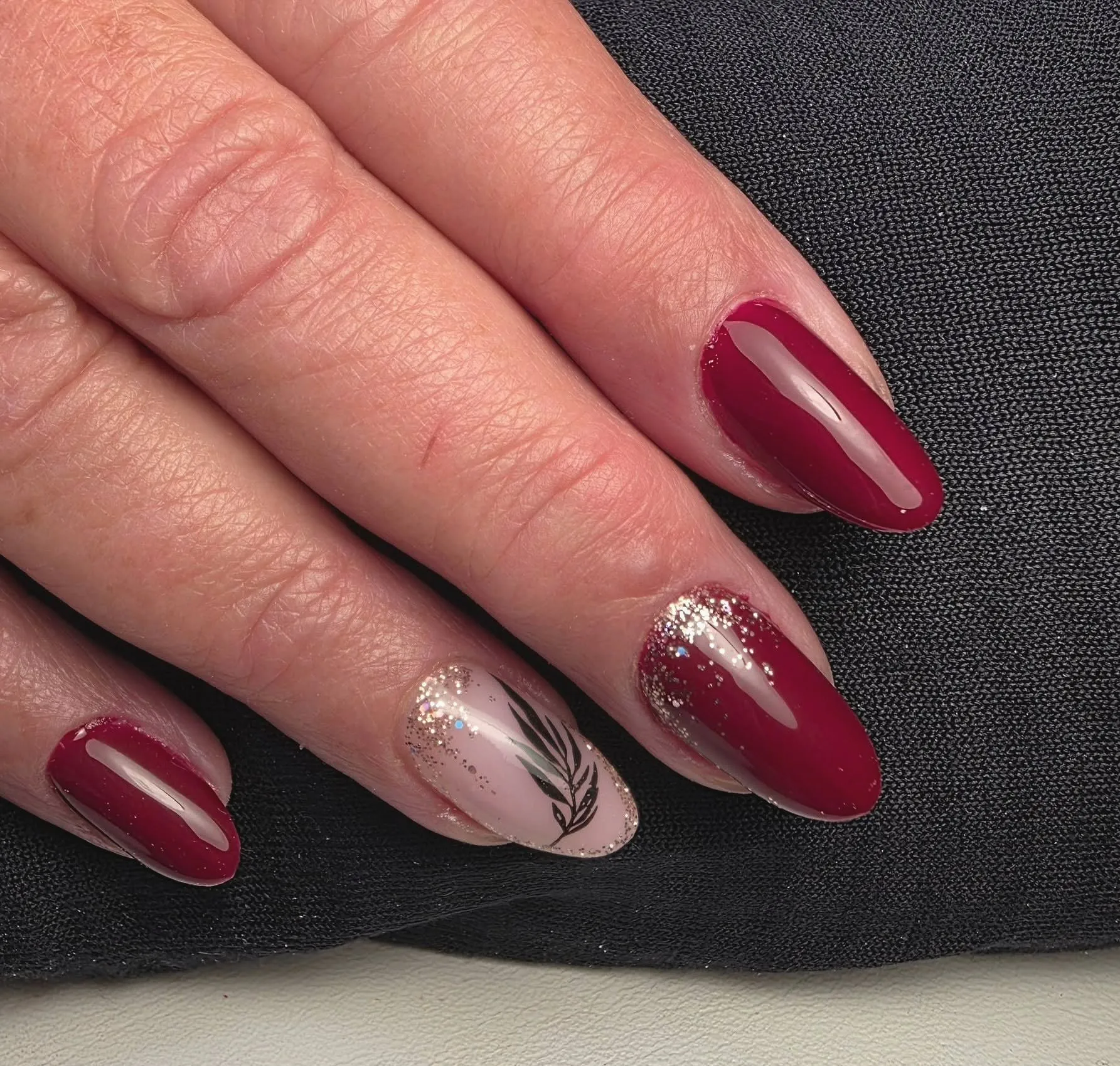 Bordeauxrode nagels, één nude nagel met een getekend zwart blad en één met glitter