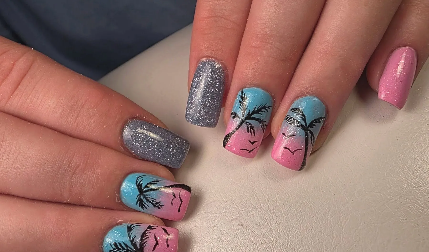 Nagels in blauw en roze met getekende palmbomen bij zonsondergang