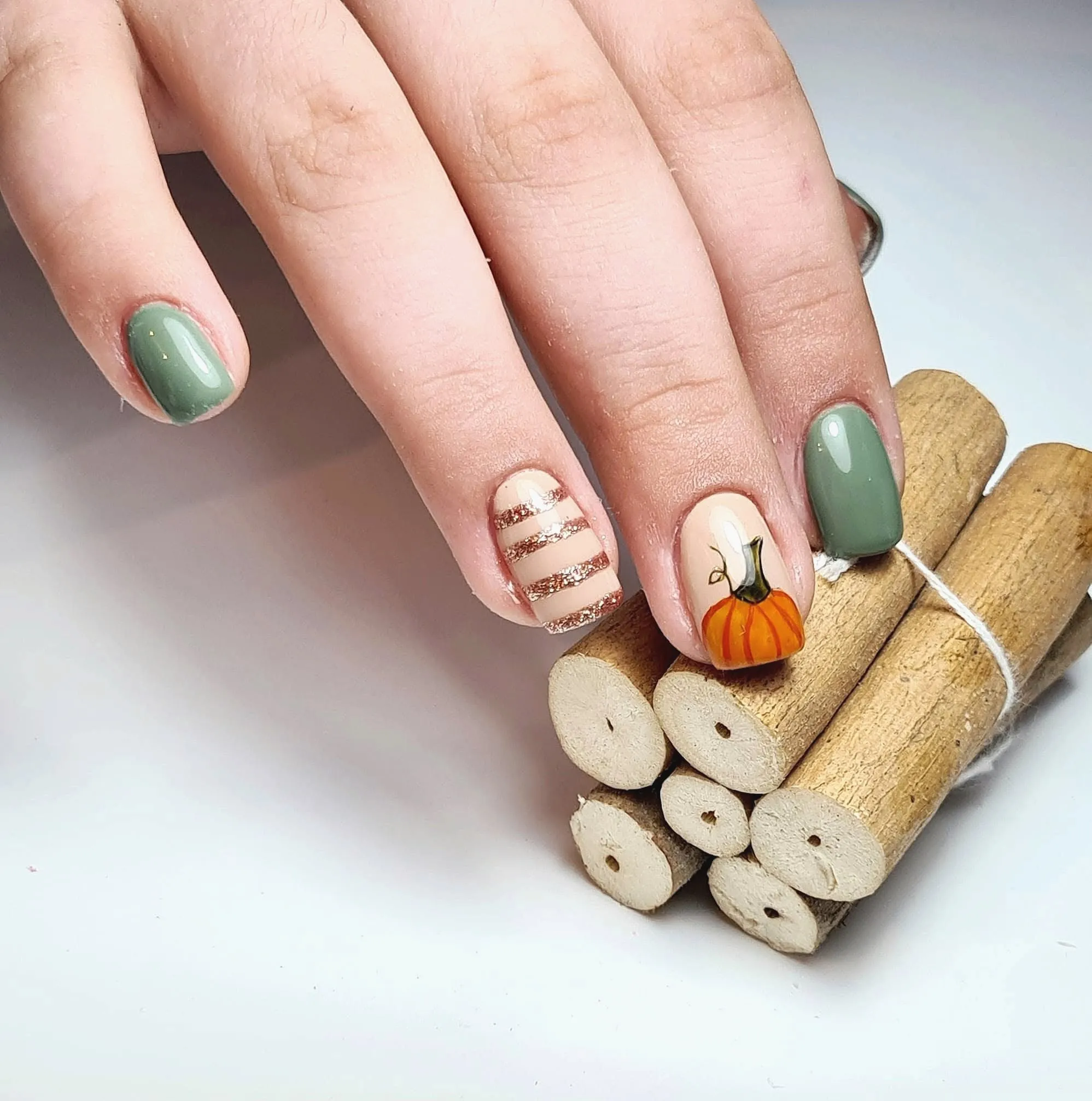 Korte saliegroene nagels, een nagel met glitterstrepen en een met een getekende pompoen